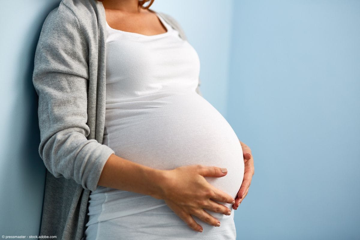 Mid-section portrait of unrecognizable woman during last months of pregnancy holding her belly gently standing against wall in blue room | Image Credit: © pressmaster - stock.adobe.com