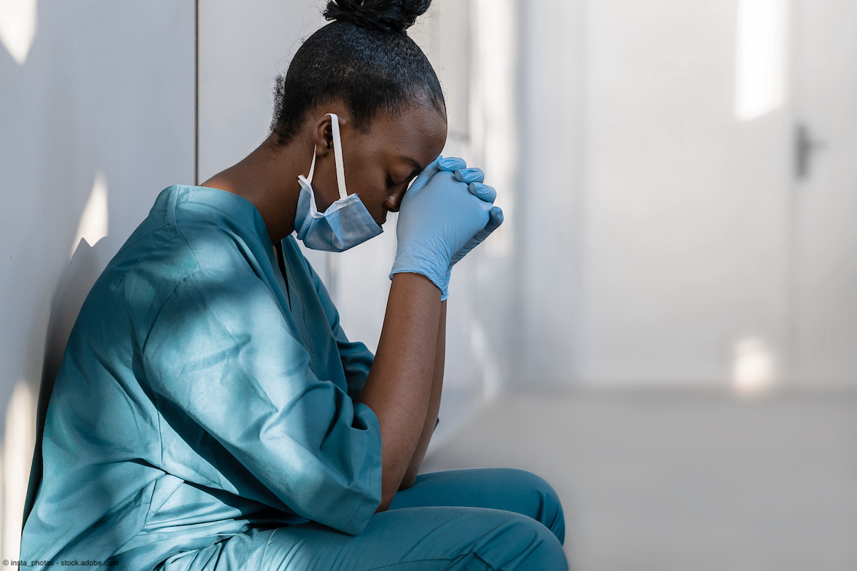 Black female doctor crouched against a wall and leaning their head on their hands